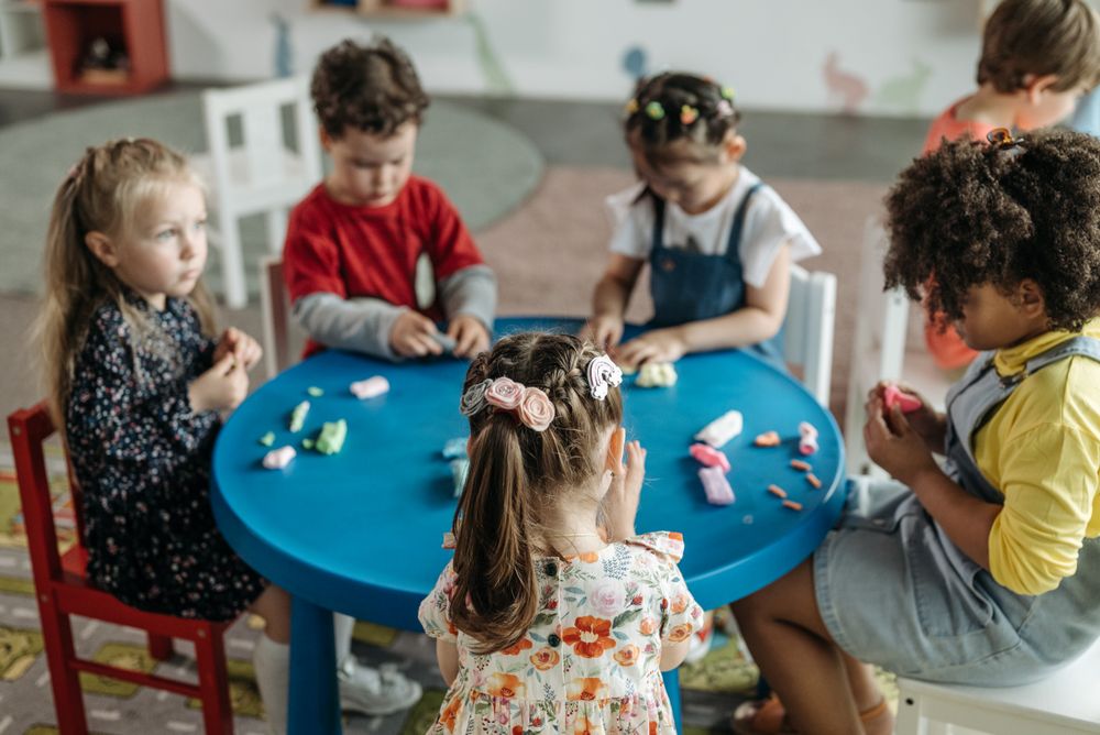 Preschool children shaping clay together at a classroom table
