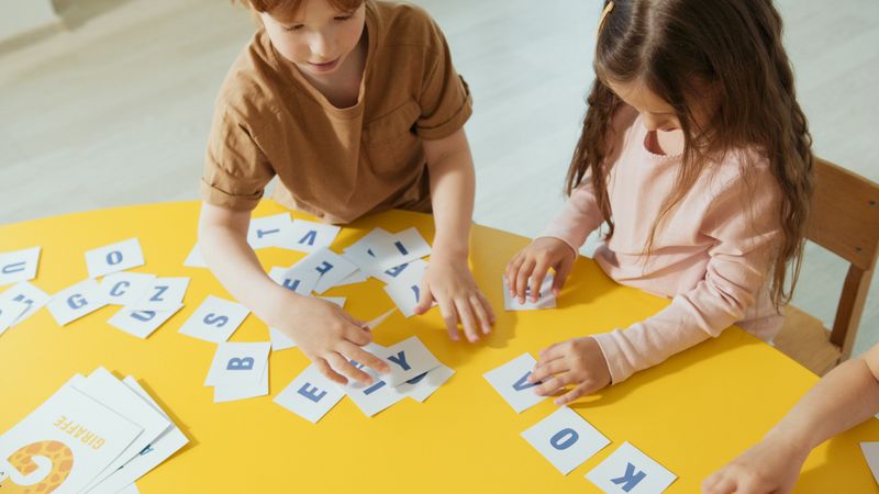 Two children holding alphabet cards at a yellow table